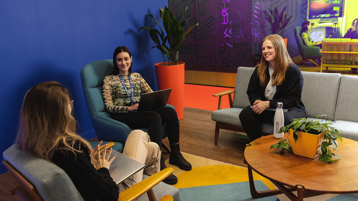 Three female employees in a colorful office chatting with their laptops. 